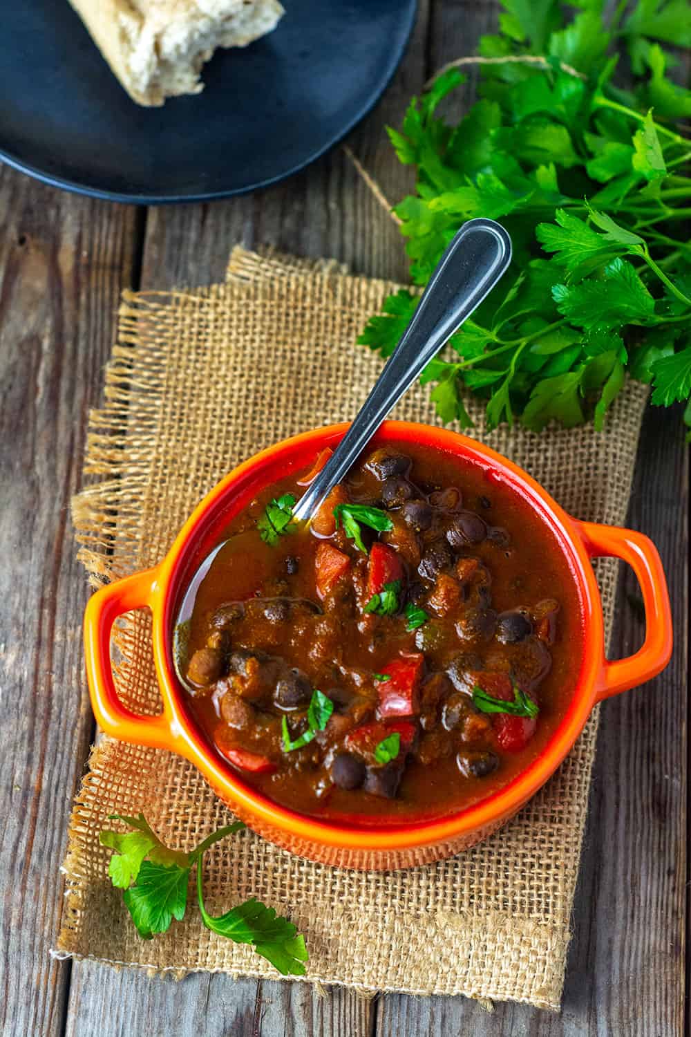 Overhead Black Chickpeas Stew with tomatoes, bell pepper, onion in a vegetable broth, served in a red dish on a wooden background garnished with parsley