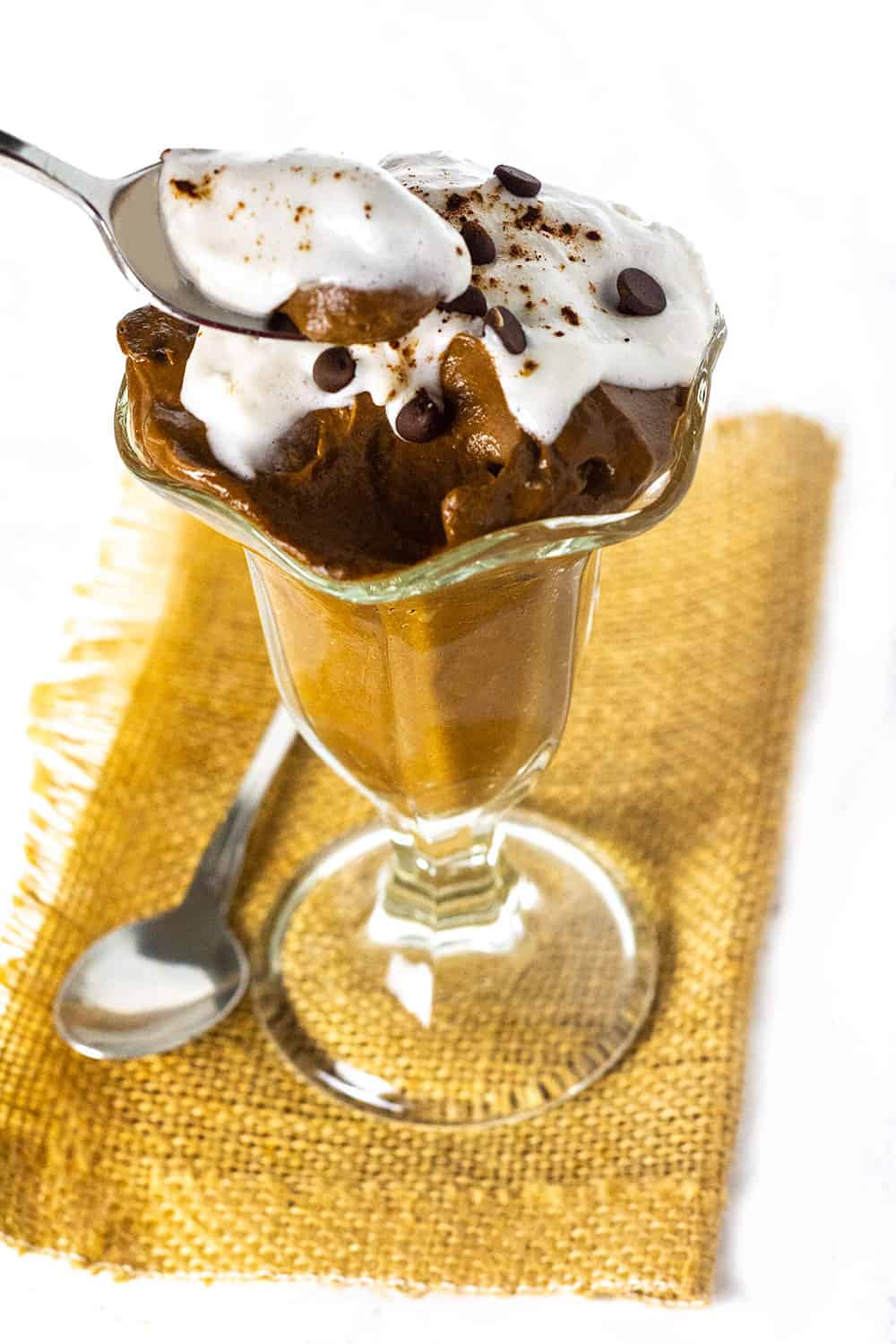 Vegan carob mousse in a glass showing a scooped out portion of the mousse on a spoon.