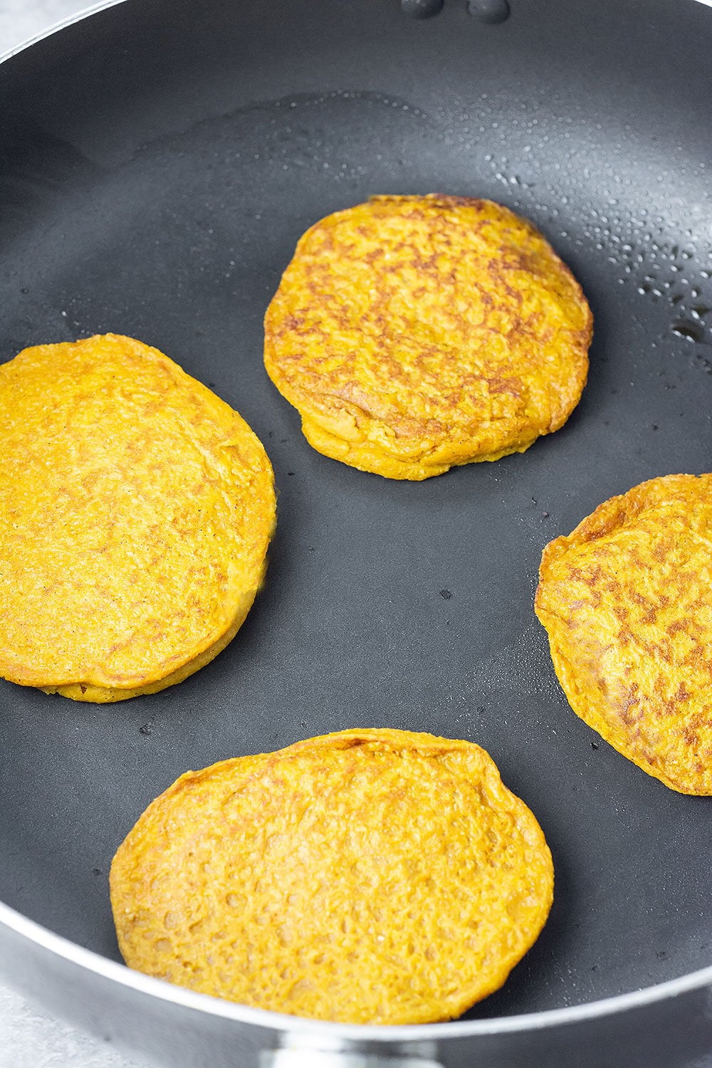 vegan pumpkin pancakes in the skillet being cooked