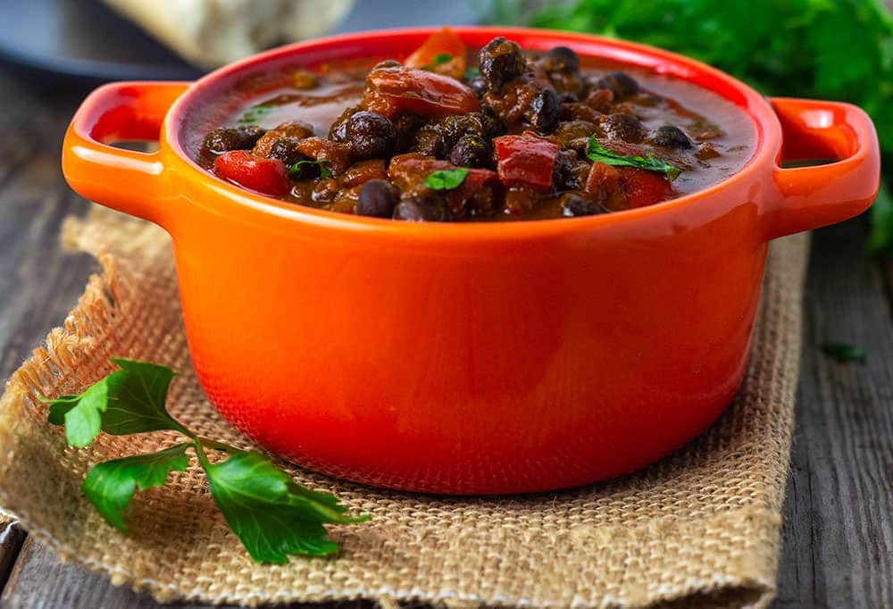 Black chickpea stew, close up photo showing black chickpeas, tomatoes, red bell pepper, garnish with fresh green parsley in a red serving dish
