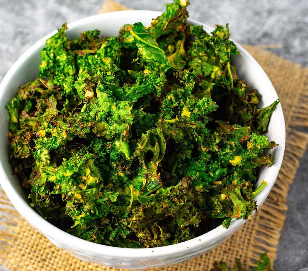 Overhead Air fryer kale chips in a white bowl on a burlap napkin on a gray marble background