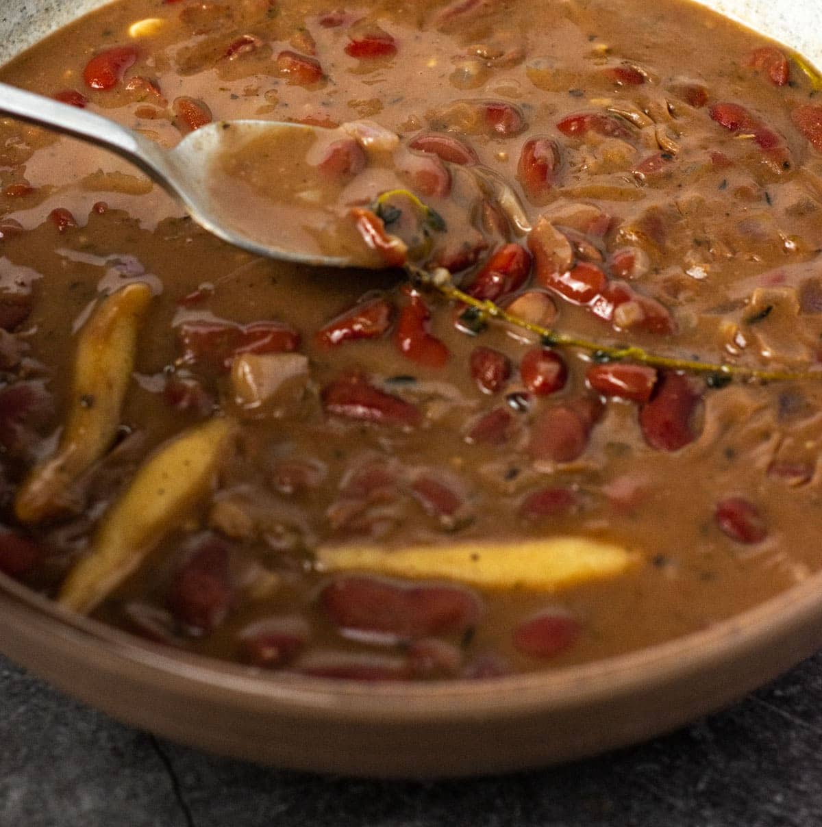 Vegan Jamaican stew peas in a beige bowl, with a spoonful of stew peas with dumplings