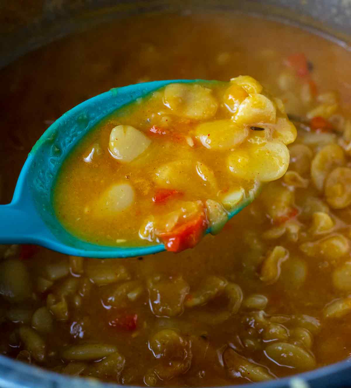 blue serving spoon holding cooked lima beans over the instant pot