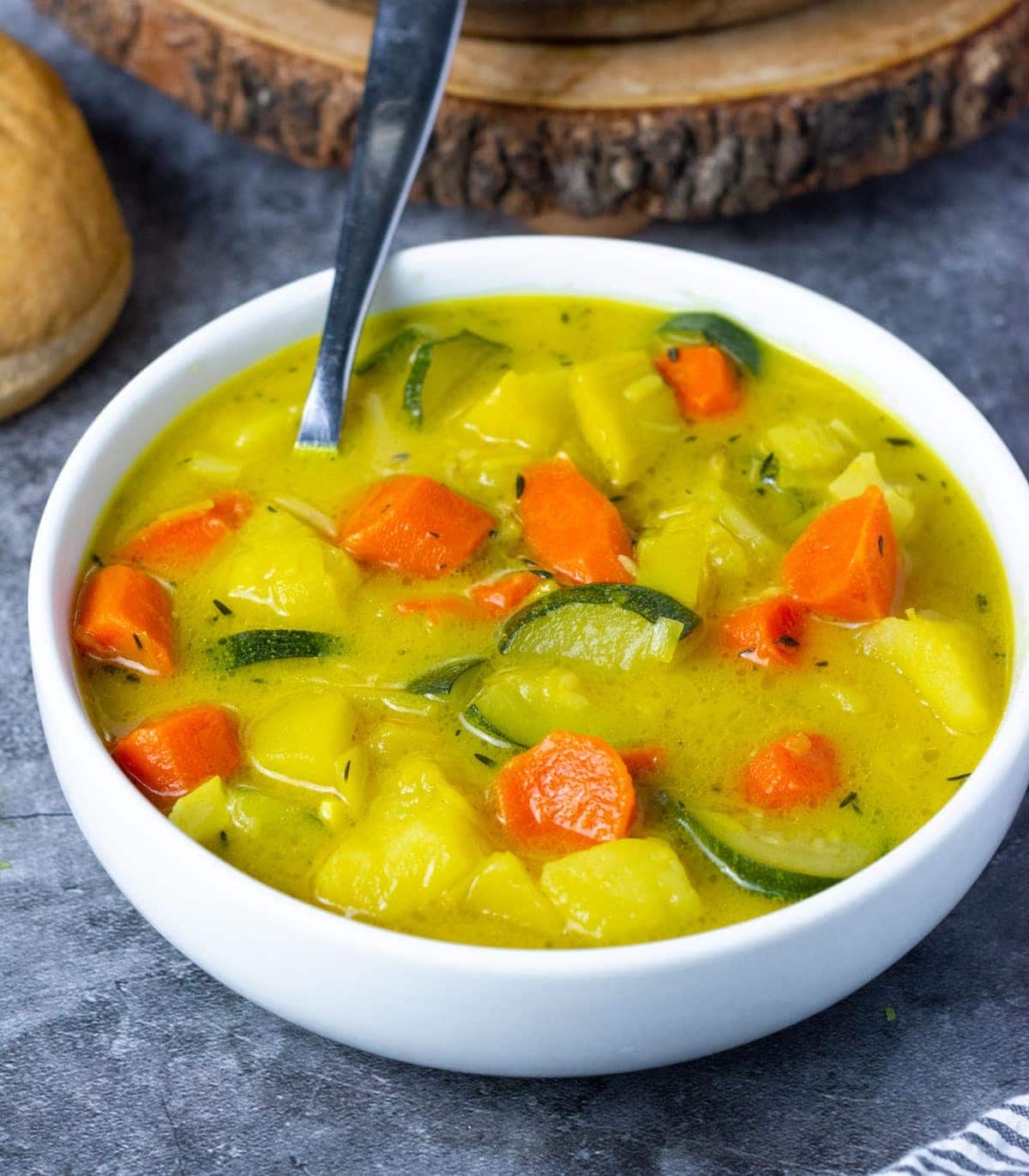 Potato leek carrot soup in a white bowl with a spoon on a grey background