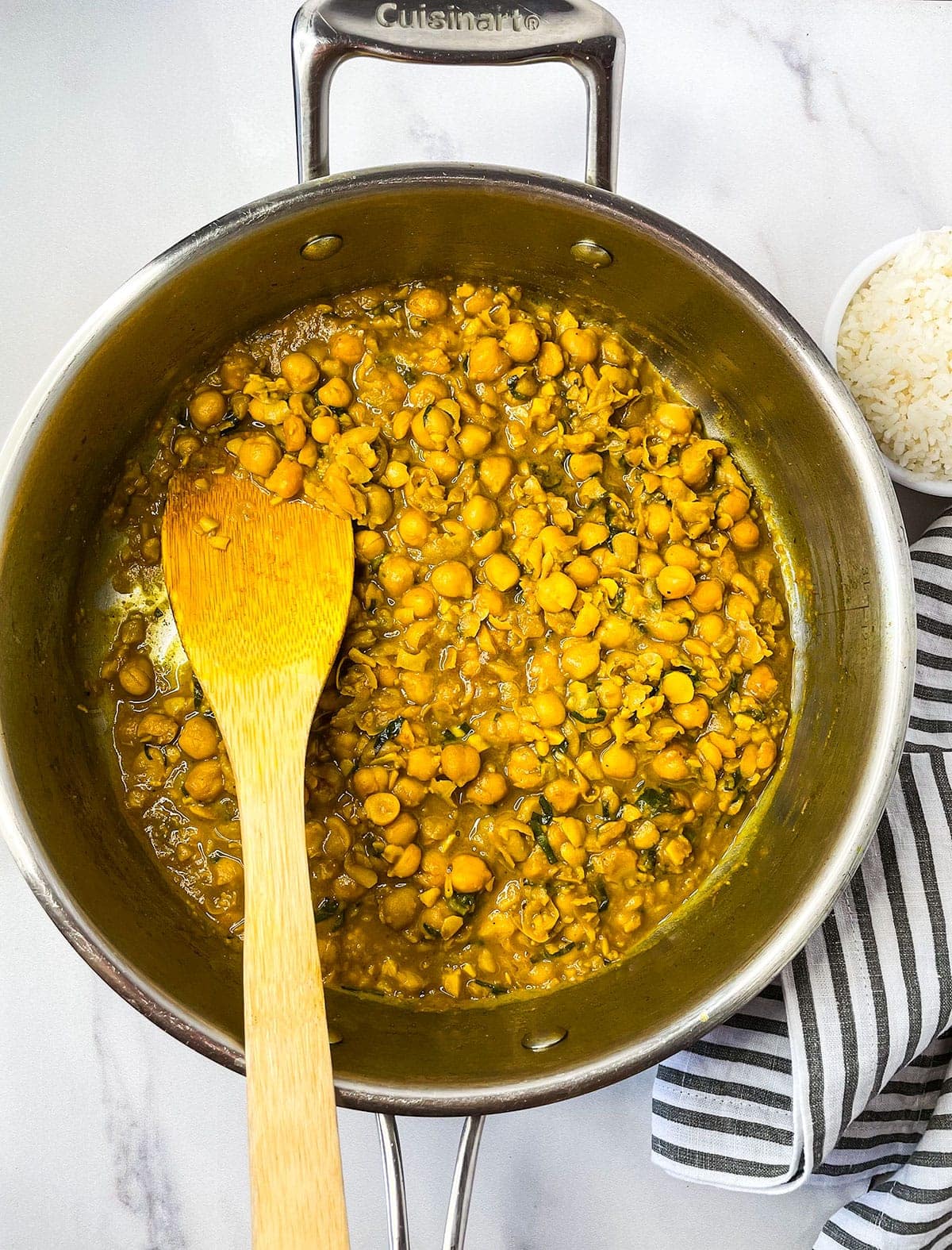 chickpea curry in a saucepan with a wooden spoon on a white background