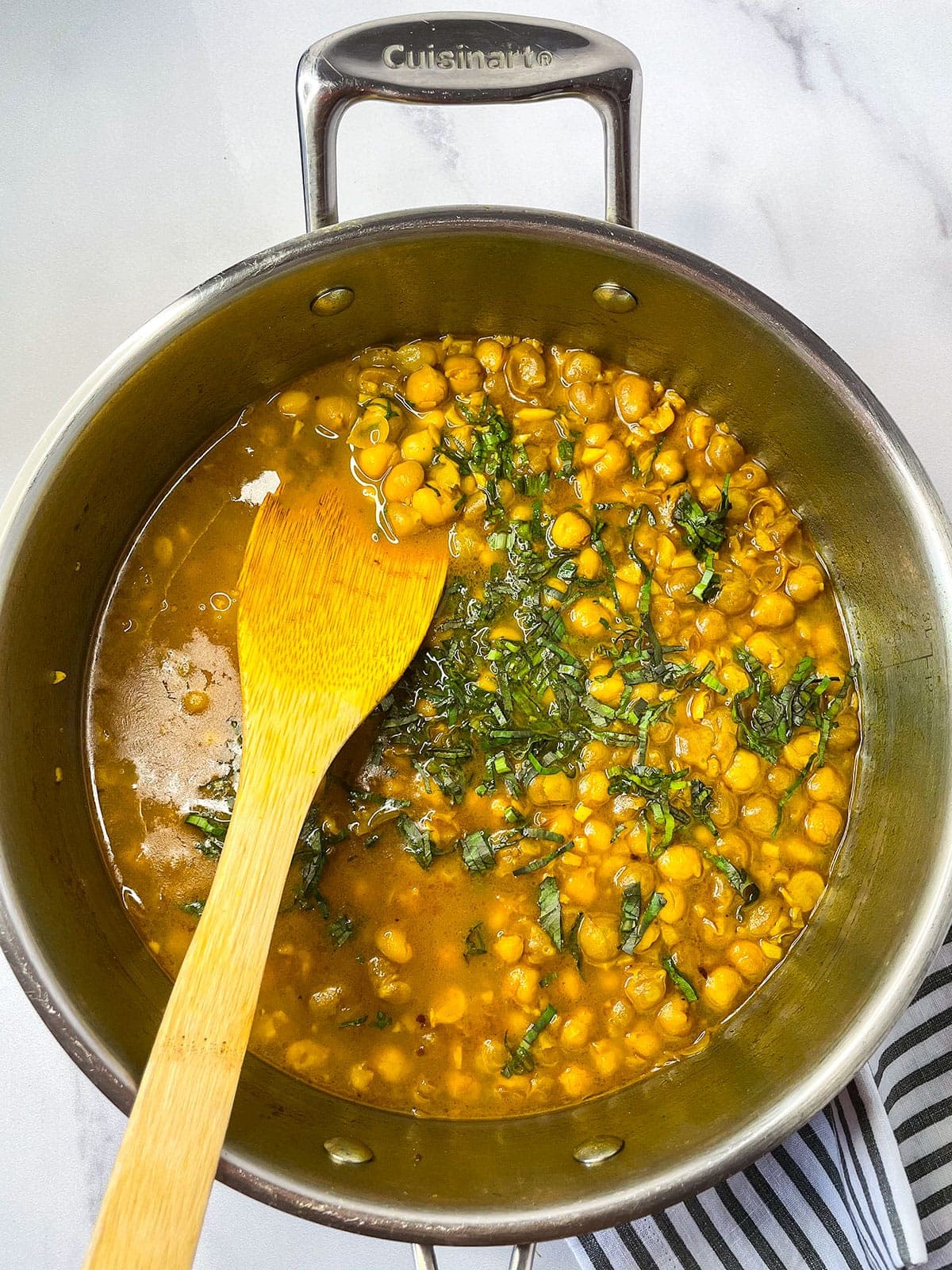 Curry chana cooking in saucepan with wooden spoon stirring