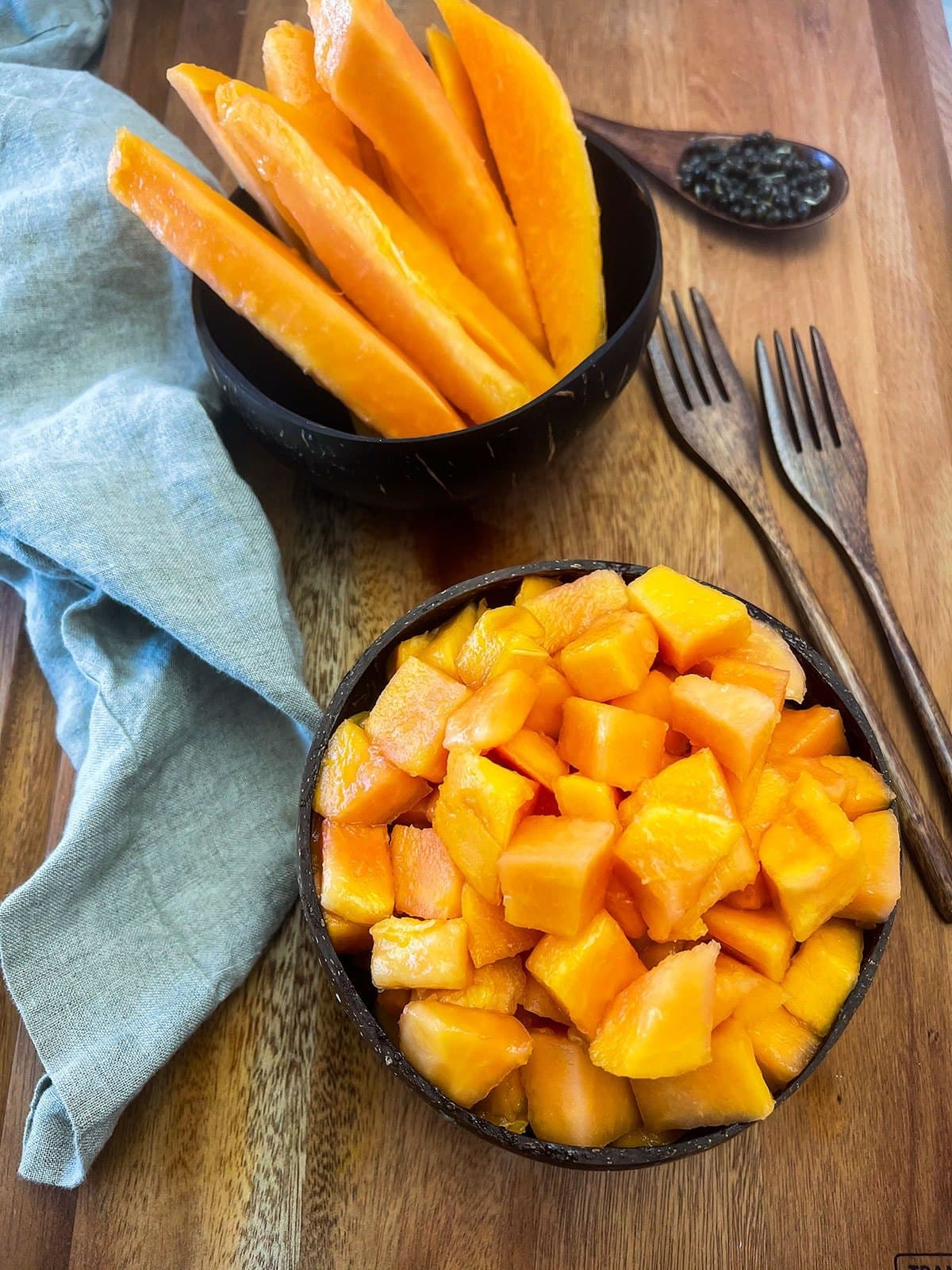 How To Cut A Papaya showing papaya cubes in a bowl and spears in a brown background with wooden utensils