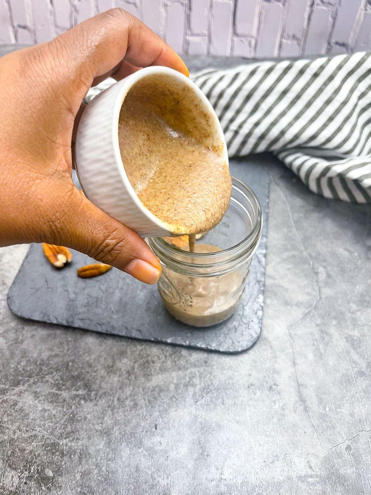 pecan butter pouring into a glass container for storage