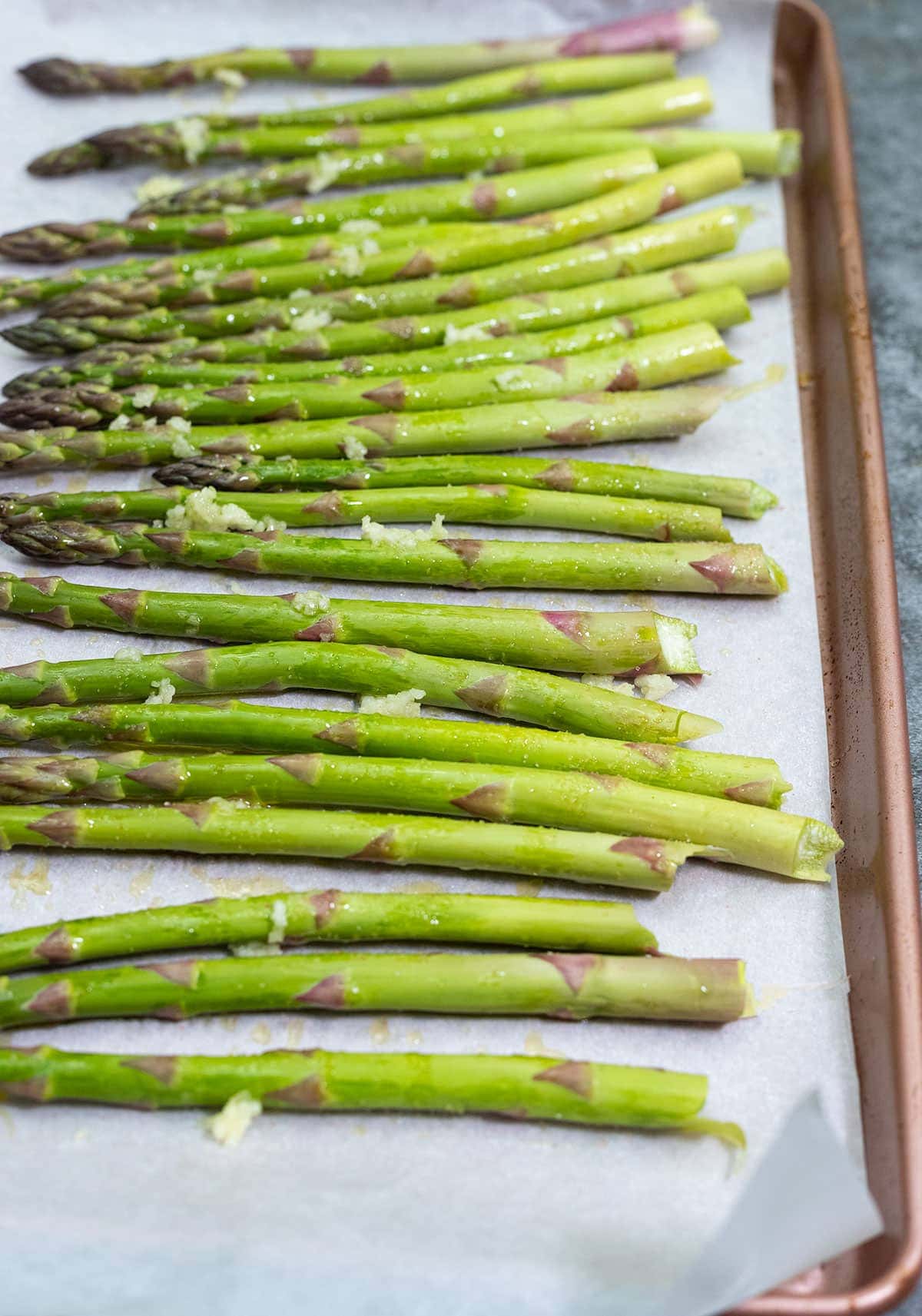seasoned asparagus on a baking tray with minced garlic