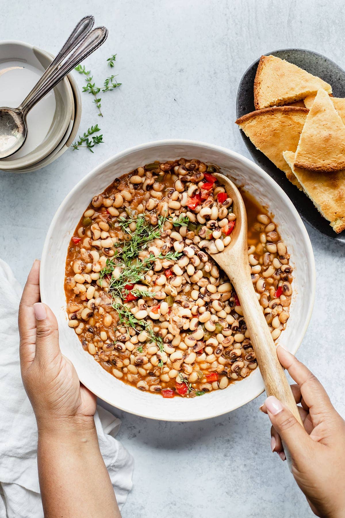 Bowl of vegan southern black-eyed peas being held with one hand and the other with a. spoon in the bowl on a white bowl on a white background