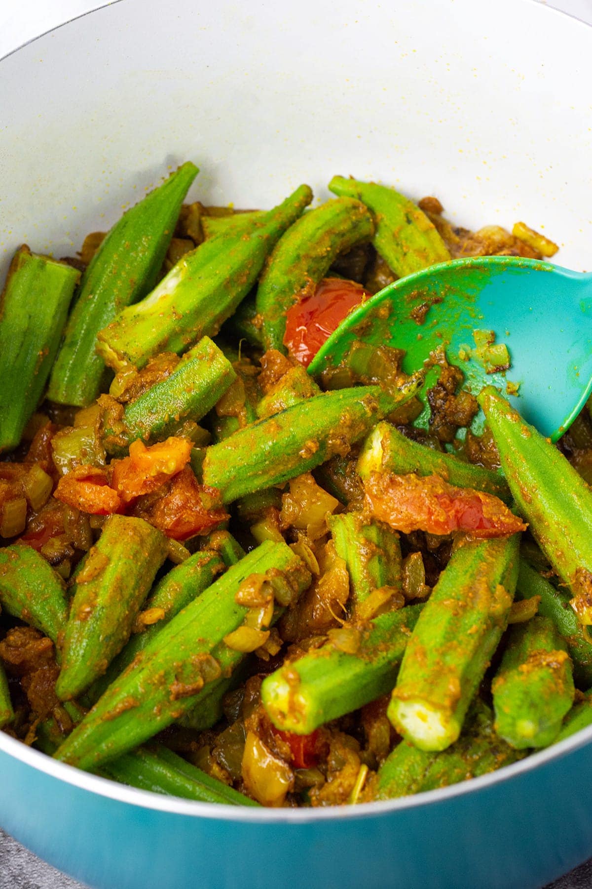 sauteed okra with onion, garlic, ginger, tomato in a large blue pot with a blue spoon