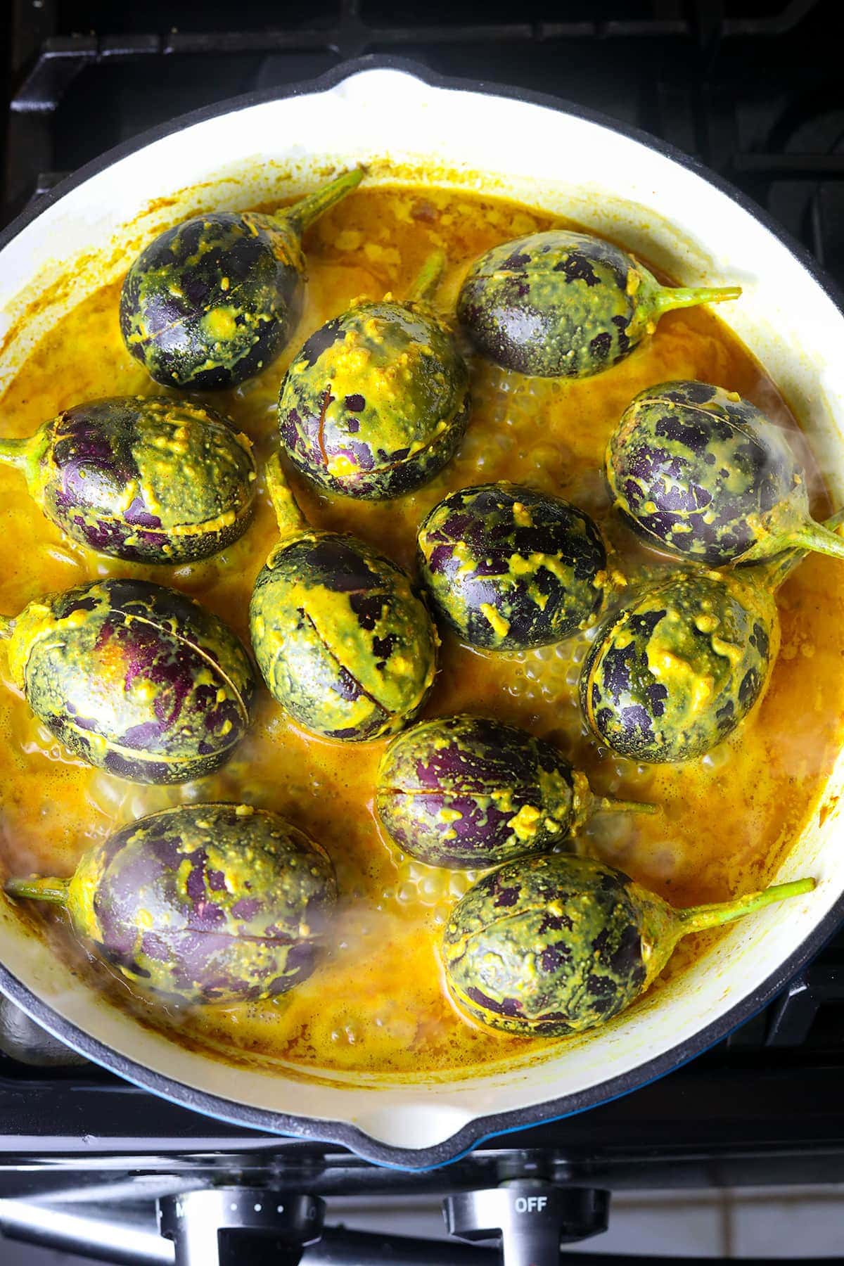 cooking baby eggplant in coconut curry in a white skillet on stove