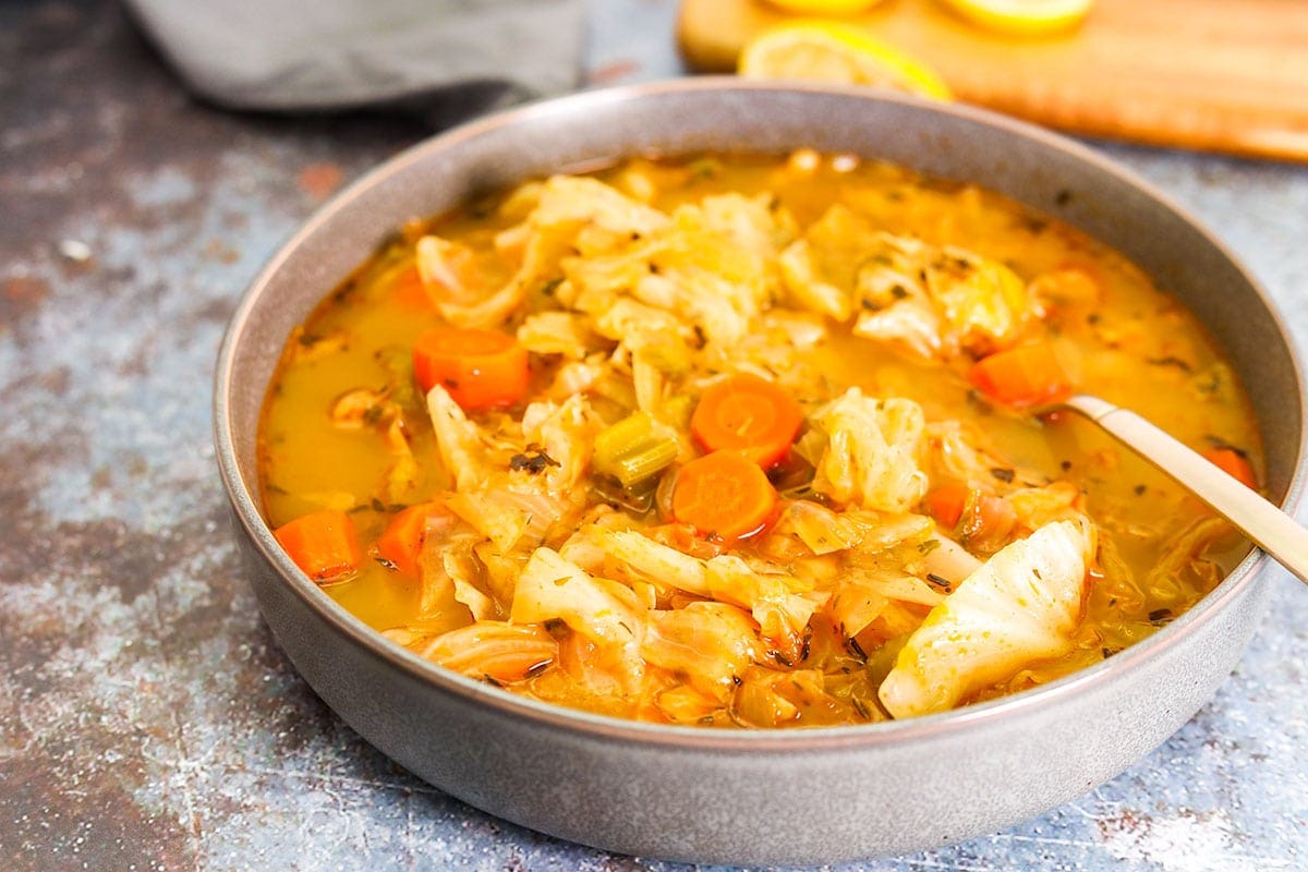 vegan cabbage soup recipe in 2 white bowls on a grey background, garnished with lime slices, scallion