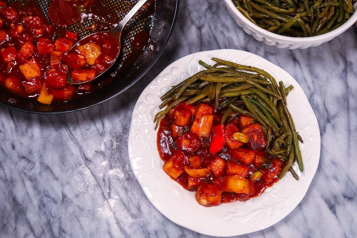 wide angle view of sweet and sour tofu with green beans on a white plate in the middle