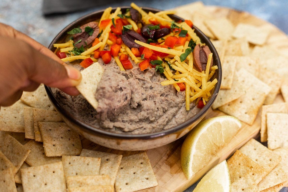 taking a scoop of black bean hummus from the bowl of hummus with a crackers