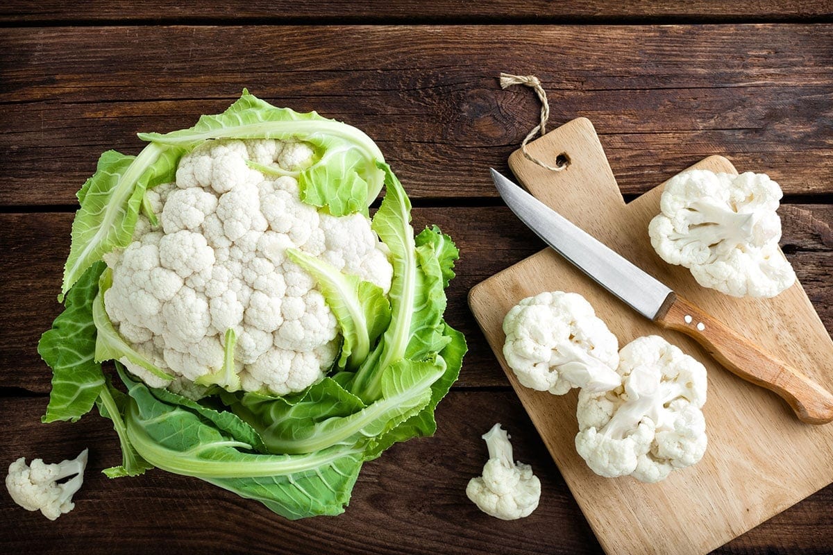 cauliflower whole and florets on a wooden cutting board