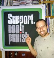 Amit from SSDP Israel standing in front of a Support Don't Punish poster.