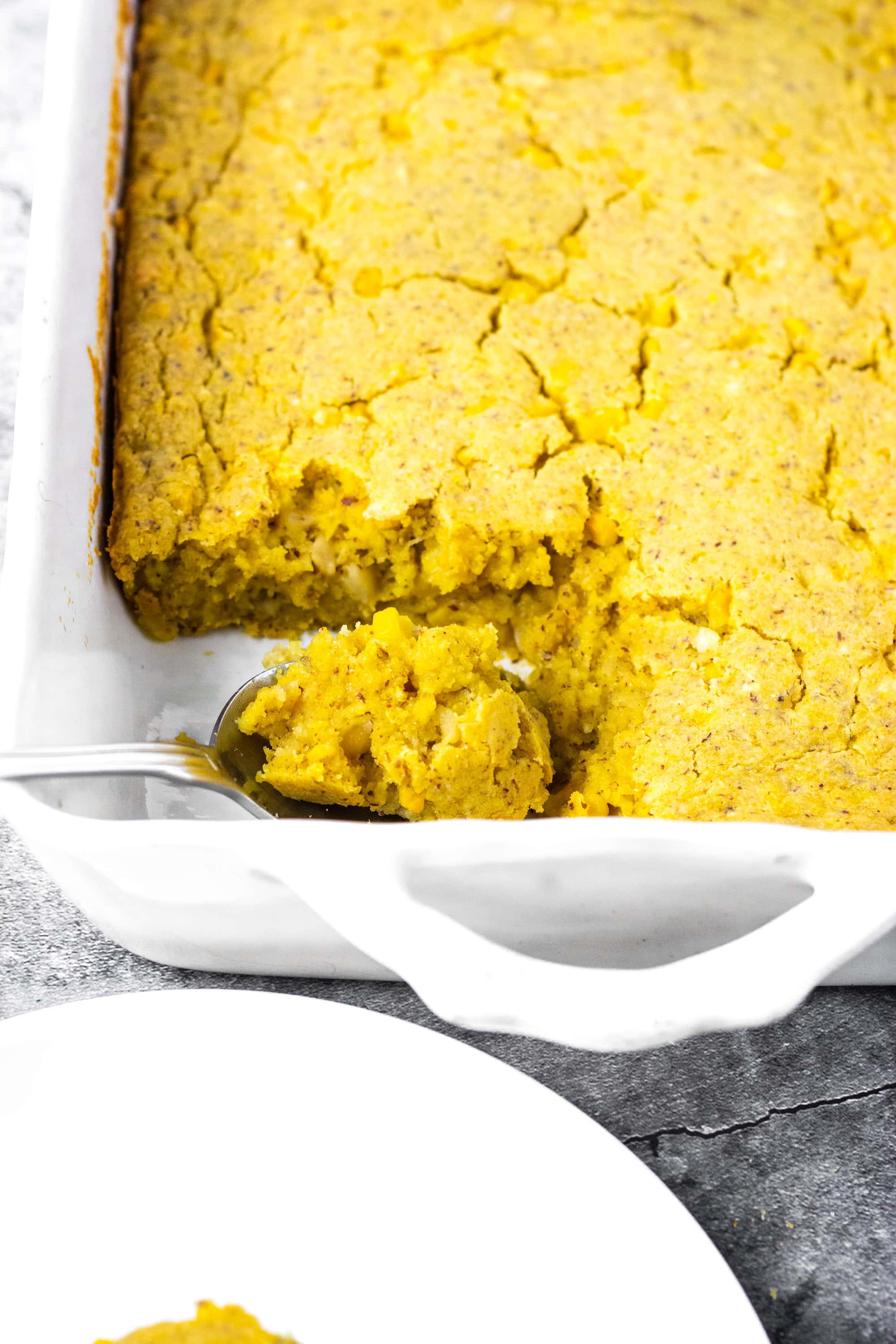 Vegan Gluten-Free Cornbread Casserole overlay in a white casserole pan with a spoonful of cornbread casserole