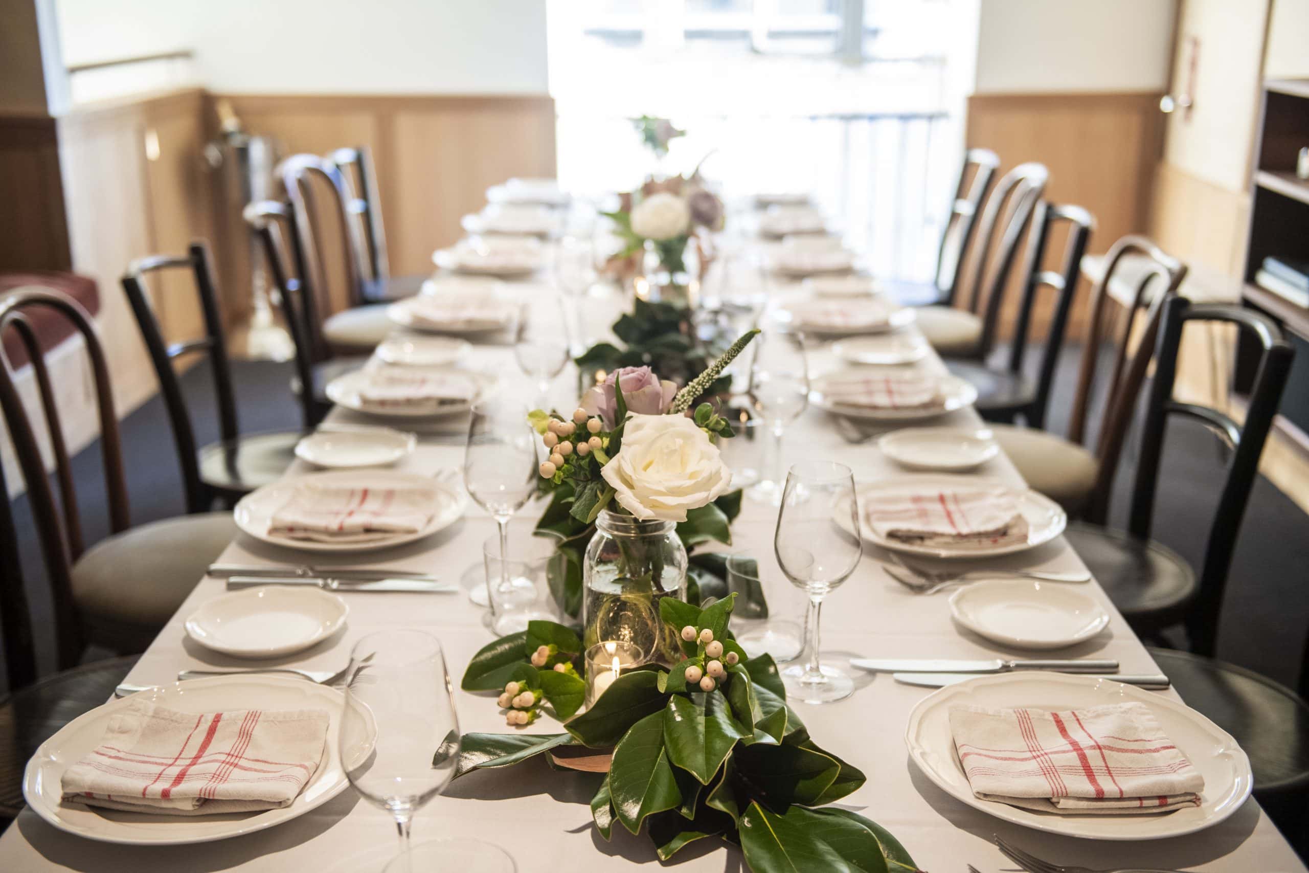 A long table set ready for a special private event at Hotel Kinsley. With 14 formal place settings and beautifully arranged centrepiece of foliage, cream roses and candles, the table in the mezzanine venue is perfect for intimate or corporate gatherings.