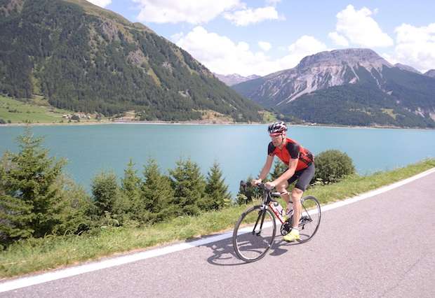 A road cyclist on a paved road alongside a lake in the mountains