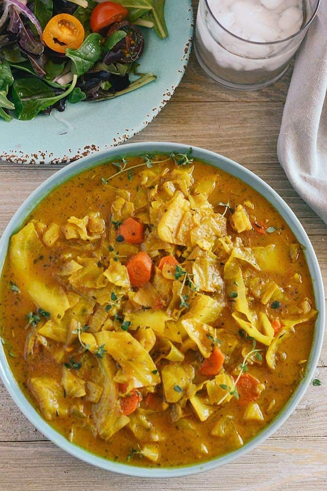 Curry Cabbage in a green bowl, overhead shot with salad on a plate and water