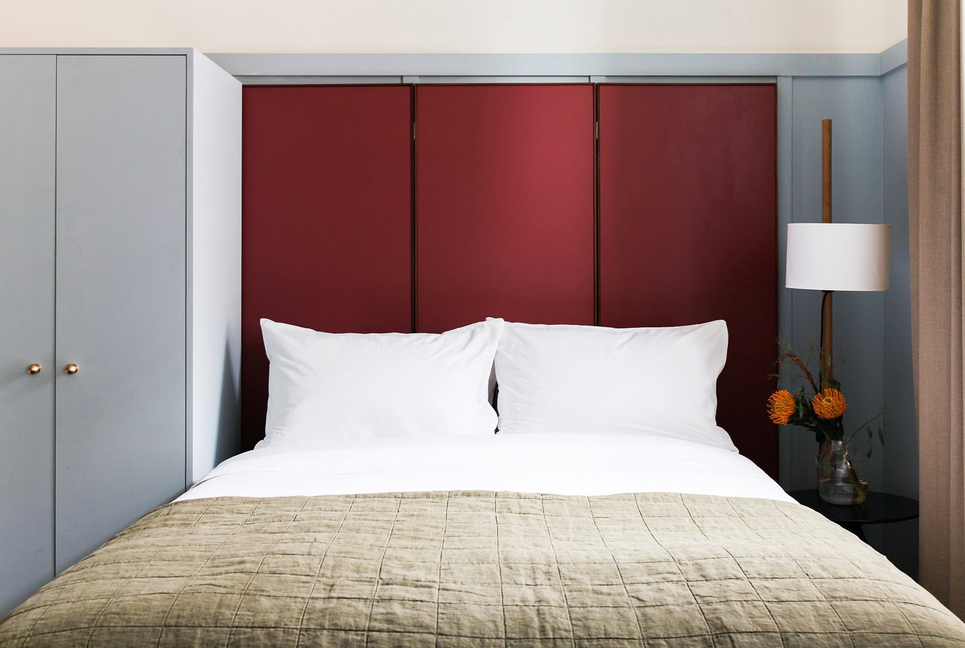 One of the queen size beds with fun, oversized headboard in Hotel Kinsley's Double Queen Guest Room at the iconic 301 Wall Street Location. With luxury linens, minimalist bedside stand, modern floor lamp, and practical full size closet.