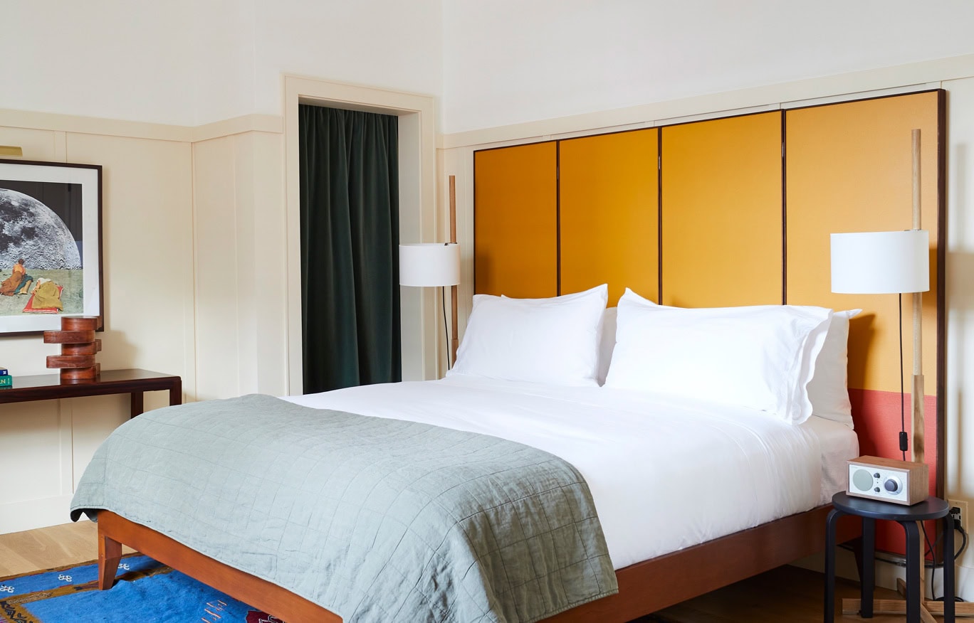 A bright and airy Standard King Guest Room at Hotel Kinsley's 301 Wall Street Location. Featuring modern king size bed in with oversized headboard and luxury linens, intentionally placed on a royal blue Turkish Rug.