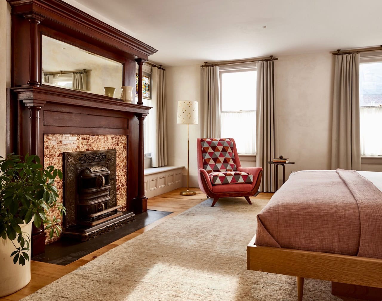 A spacious and sun-soaked Luxury King Suite at Hotel Kinsley's John Street location. With a traditional grand fireplace, modern handmade bed frame and lounge chair, with large windows and reading nook overlooking a private desk.