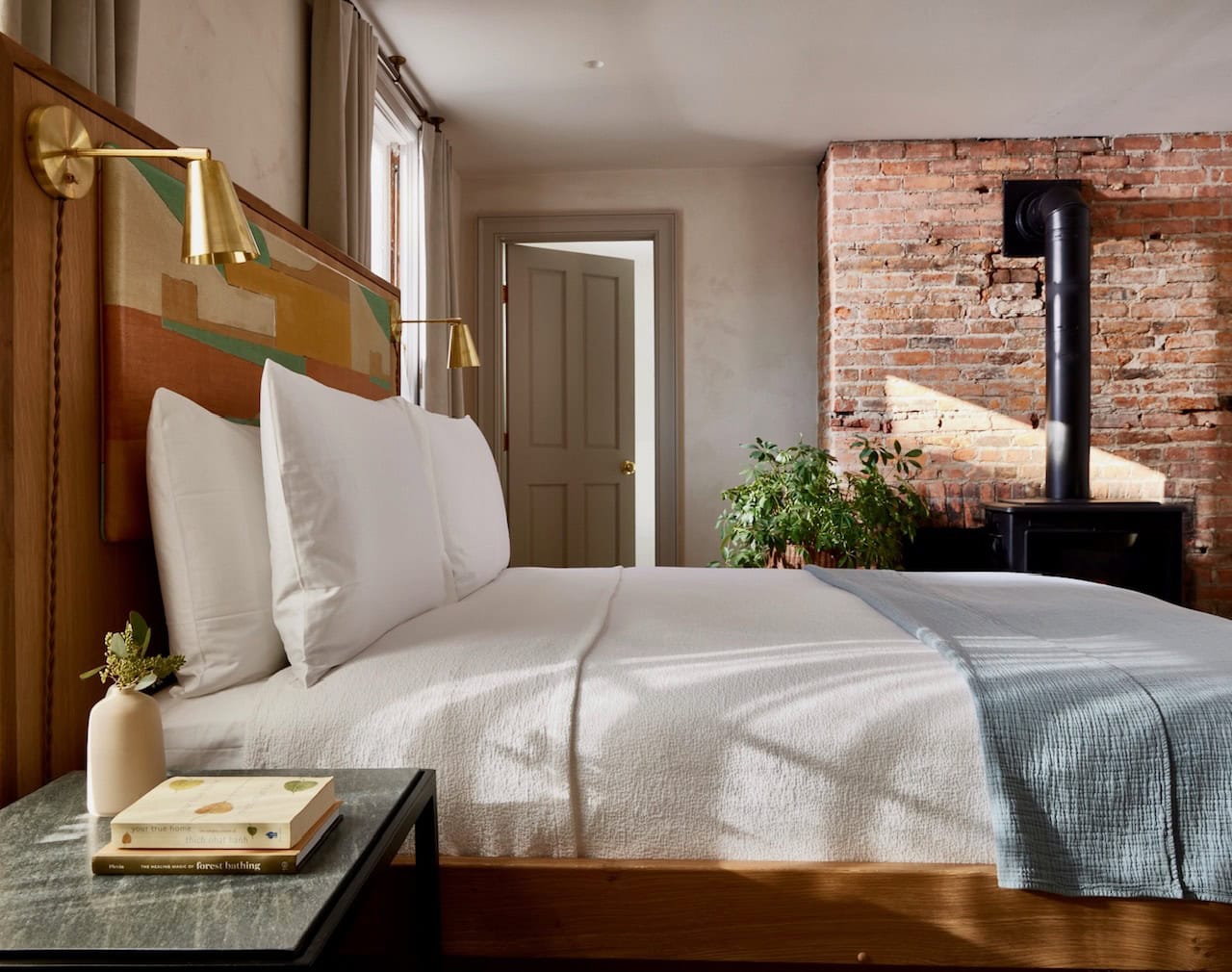 One of Hotel Kinsley's John Street Luxury Queen rooms, with original brickwork chimney and wood burner-style fireplace, making for a cozy yet modern and minimalist haven. Complete with mid century modern queen bed made with Frette linens.