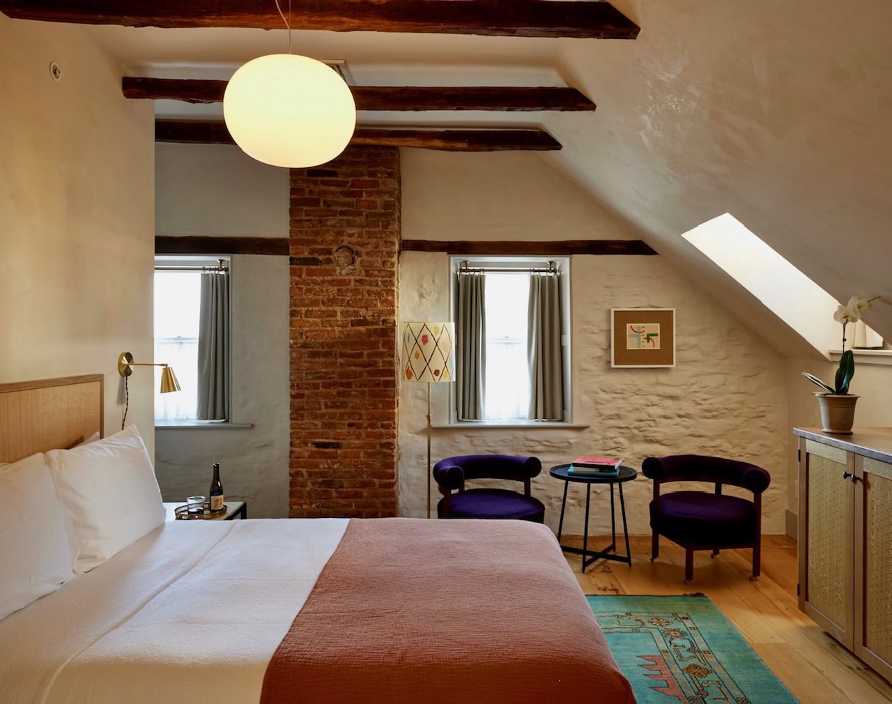 One of Hotel Kinsley's John Street Standard Queen rooms, nestled on the second floor with charming sloped ceilings and original wooden beams. Contrasted with modern and minimalist design aesthetics, custom made queen bed and cozy seating area.