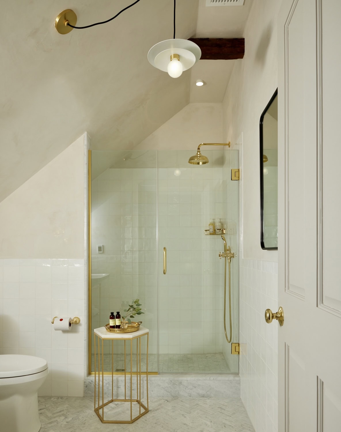 The beautifully designed shower in the loft space of Hotel Kinsley's John Street Standard Queen rooms, with pristine white tiles, modern curved edge mirror and contrasting antique brass fixtures.