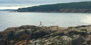 A girl jumps along boulders on the coast of acadia national park