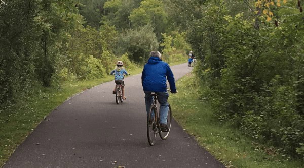 A dad and daughter ride bikes on the wide, flat and green ashuwillticook rail trail.