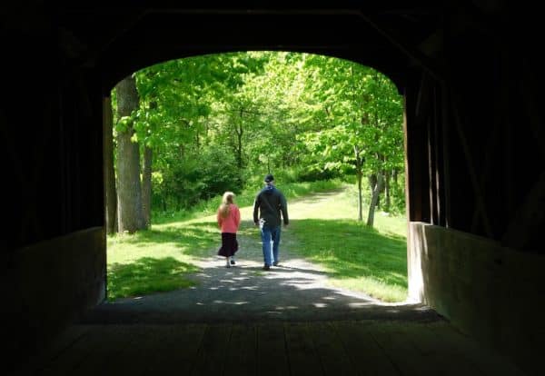 A girl and dad leaving the covered bridge on a nature trail in glimmerglass state park.