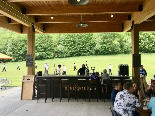 The outside bar and field behind ommegang brewery and tap house, a basebal game is happening.