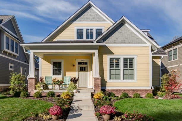cottage exterior with yellow and grey siding, white trim, grey windows, beige door, and pink-brick detail