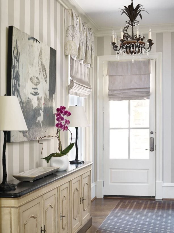 an off-white blackout roman shade covering a traditional half glass door entry