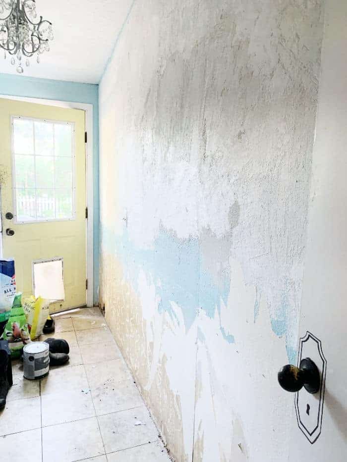 Before picture of wall with uneven texture and ripped wallpaper.