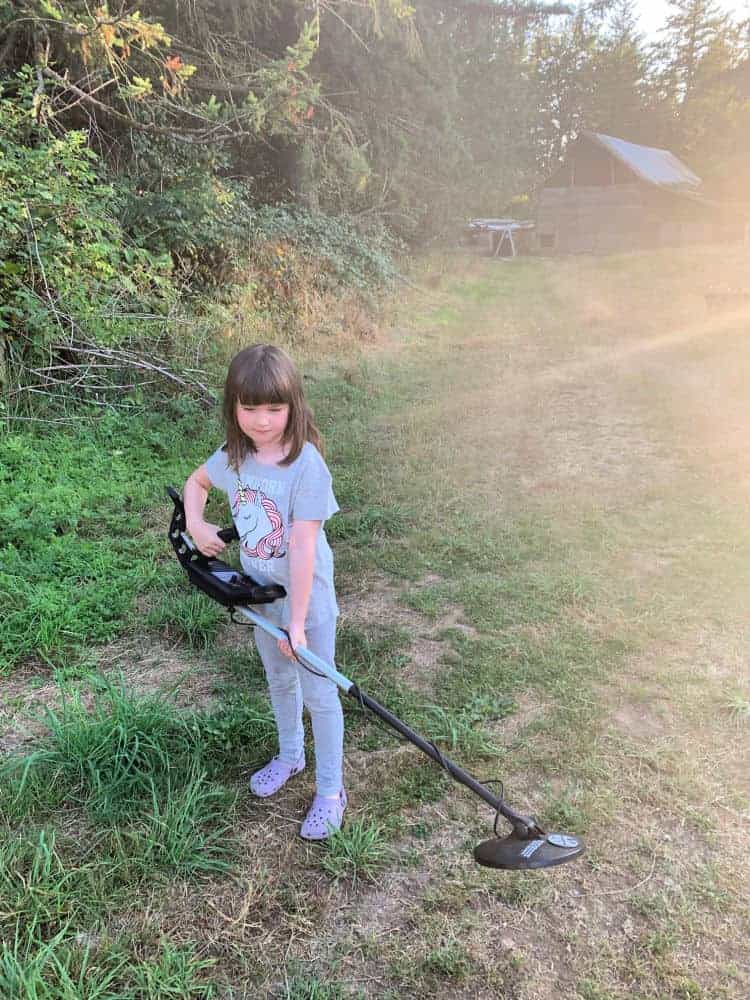 young girl holding metal detector in grassy field