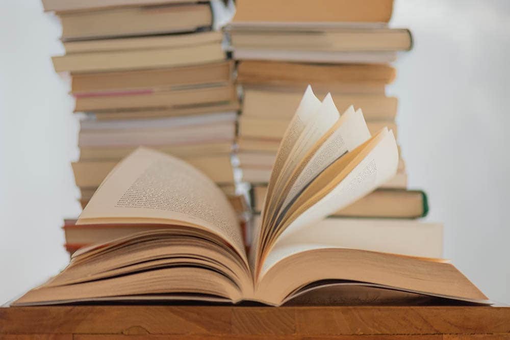 aufgeschlagenes Buch vor einem Bücherstapel