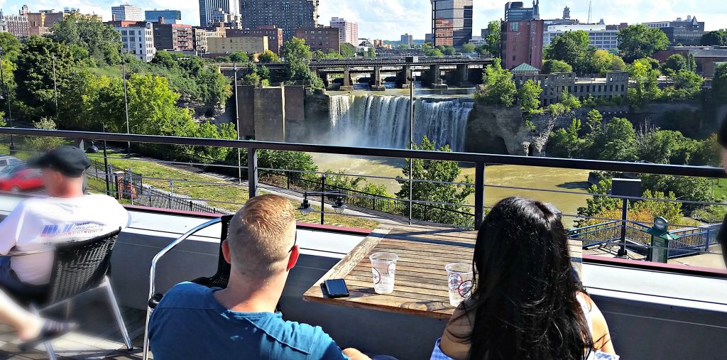 Couple looks from rooftop bar to High Falls, a waterfall in downtown Rochester, NY.