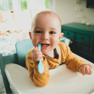 A child chomping on a spoon with their developing teeth.