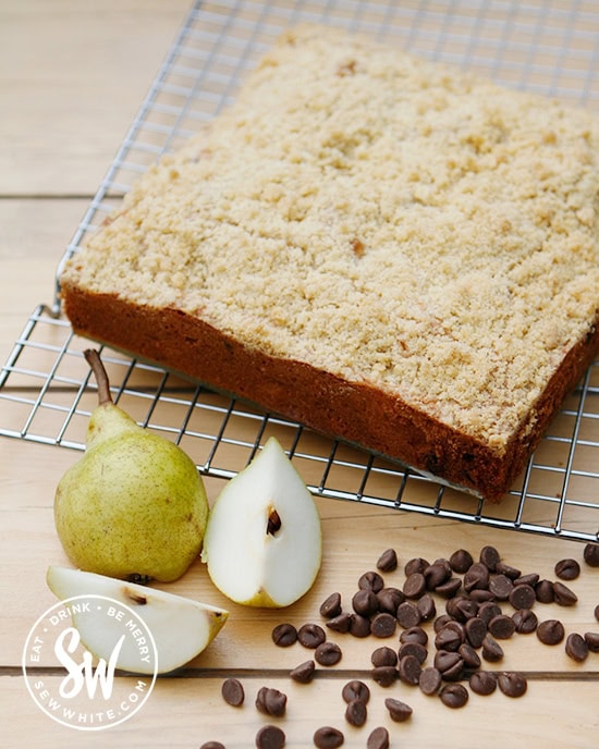 Gold brown Pear Crumble Cake with fresh pears and chocolate chips on a kitchen table