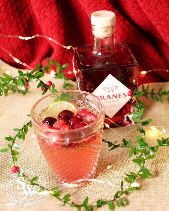 Sparkling Cranberry Ginger Cocktail made with Cranes cranberry liqueur decorated with fresh cranberries and a slice of lime. Christmas cocktail