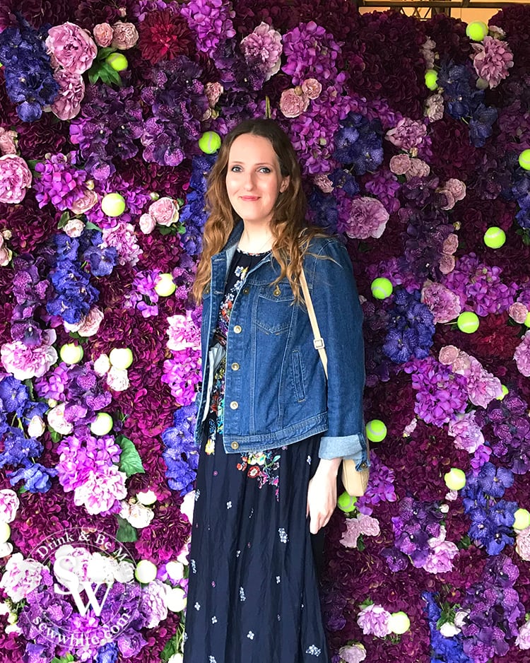 Sisley White at the dog and fox in wimbledon village at their Wimbledon inspired purple and pink flower wall studded with tennis balls.