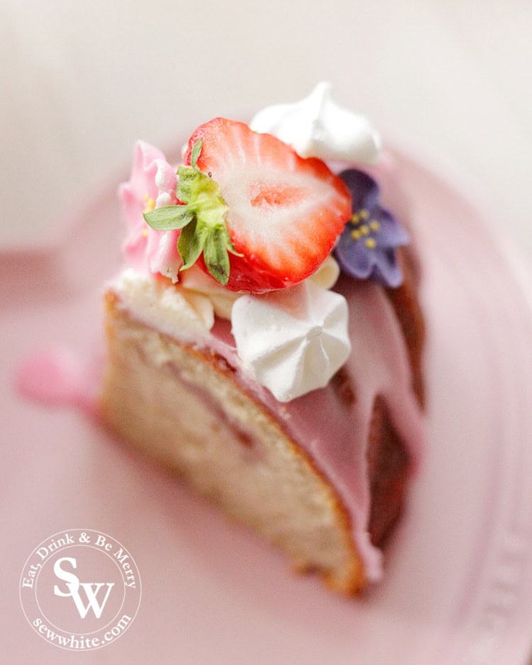 A beautiful slice of Strawberry Prosecco Cake topped with pink icing, meringues and sugar flowers.