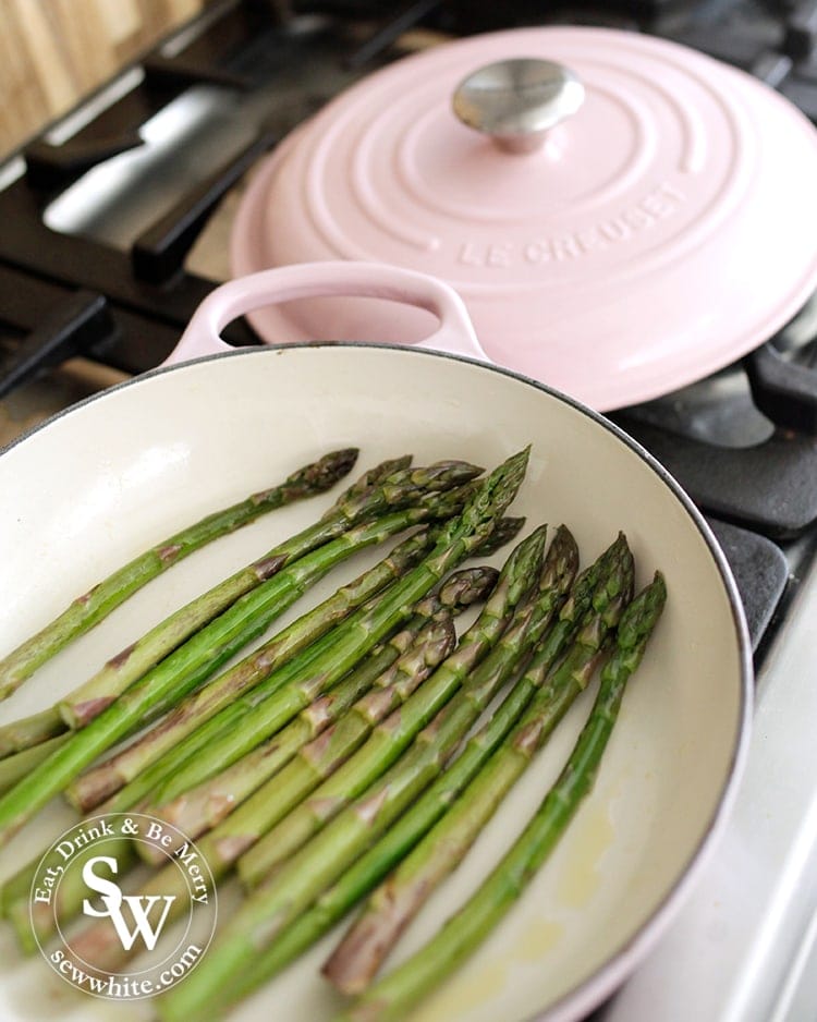 Asparagus cooking in a pink le creuset shallow casserole dish