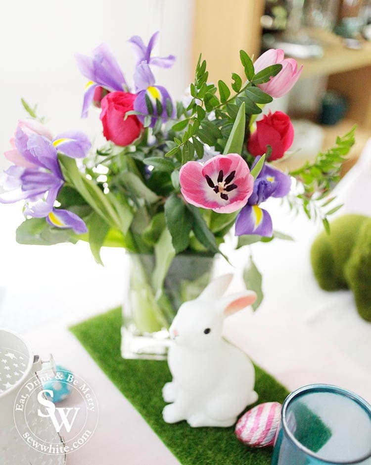 the cutest rabbit statue on fake green grass and with fresh tulips, irises, roses and greenery