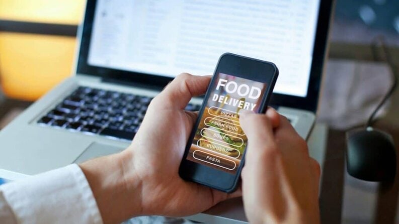 customer ordering from both hands holding cell phone in front of laptop menu on screem
