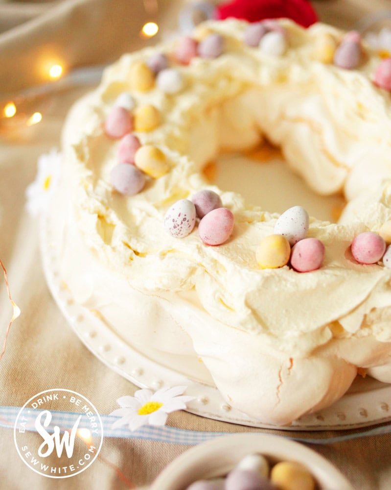 The finished Easter meringue served on a white plate, topped with cream and mini eggs